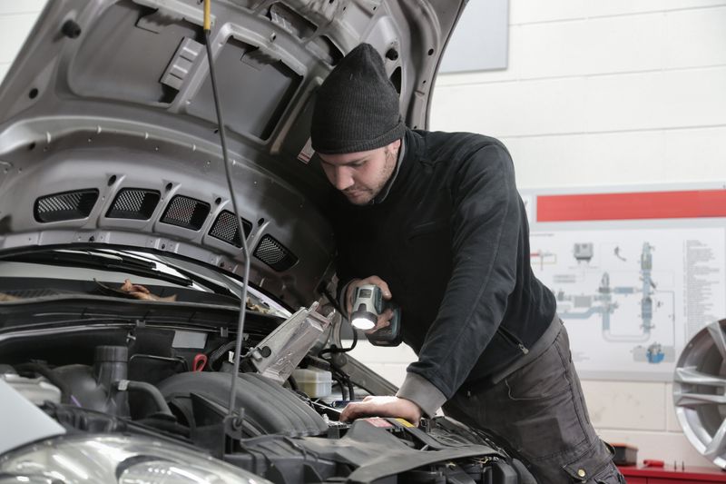 Auto technician inspecting an engine bay with a flashlight